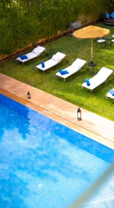 Oasis Privée Chaises longues blanches autour d'une piscine, avec un parasol au-dessus, sur une pelouse verte.