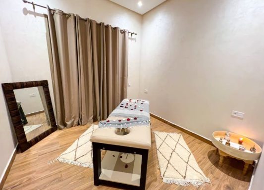 Repos Absolu Salle de massage avec table, miroir, rideaux, tapis, et bougies décoratives.