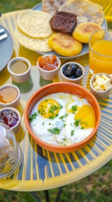Éveil Gourmand Petit-déjeuner coloré avec œufs, sauces, fruits et boissons sur une table en extérieur.