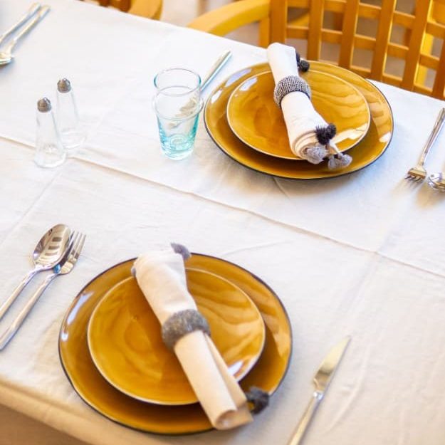 Table dressée avec des assiettes jaunes, serviettes enroulées et verres d'eau.