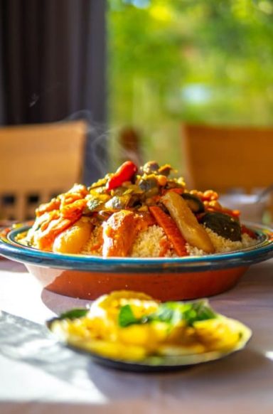 Saveurs Locales Un plat de couscous avec légumes colorés et sauce, accompagné d'une assiette de salade.